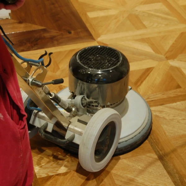 orbital sander being used on a hardwood floor with a parquet (geometric) pattern.